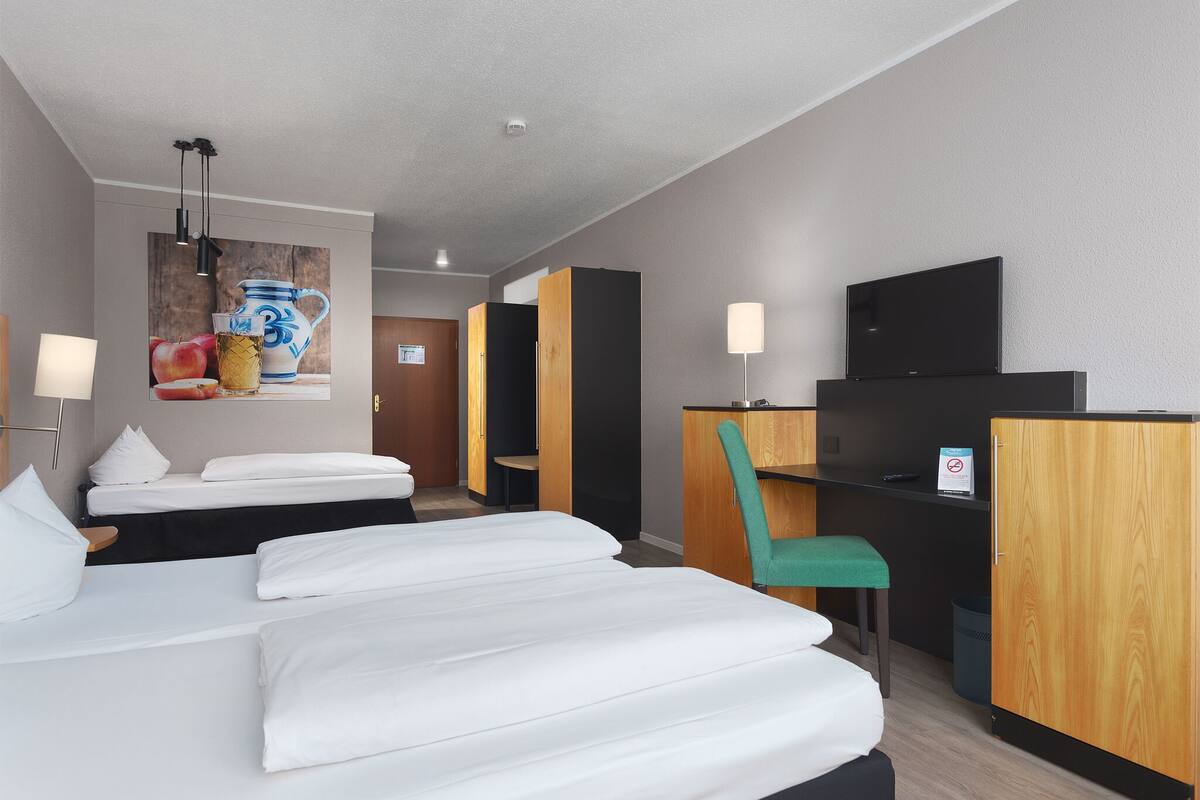 A hotel room with two beds, a desk with a chair, a television, and a painting on the wall.