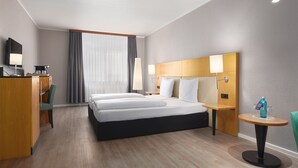 Une chambre d’hôtel avec un grand lit, un bureau avec une chaise, une télévision et une petite table avec une bouteille.