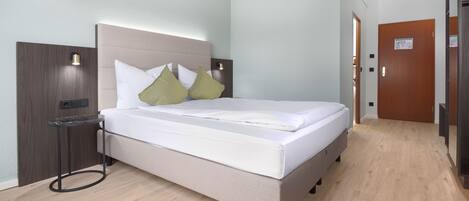Una habitación de hotel moderna con cama, mesita de noche y una puerta.
