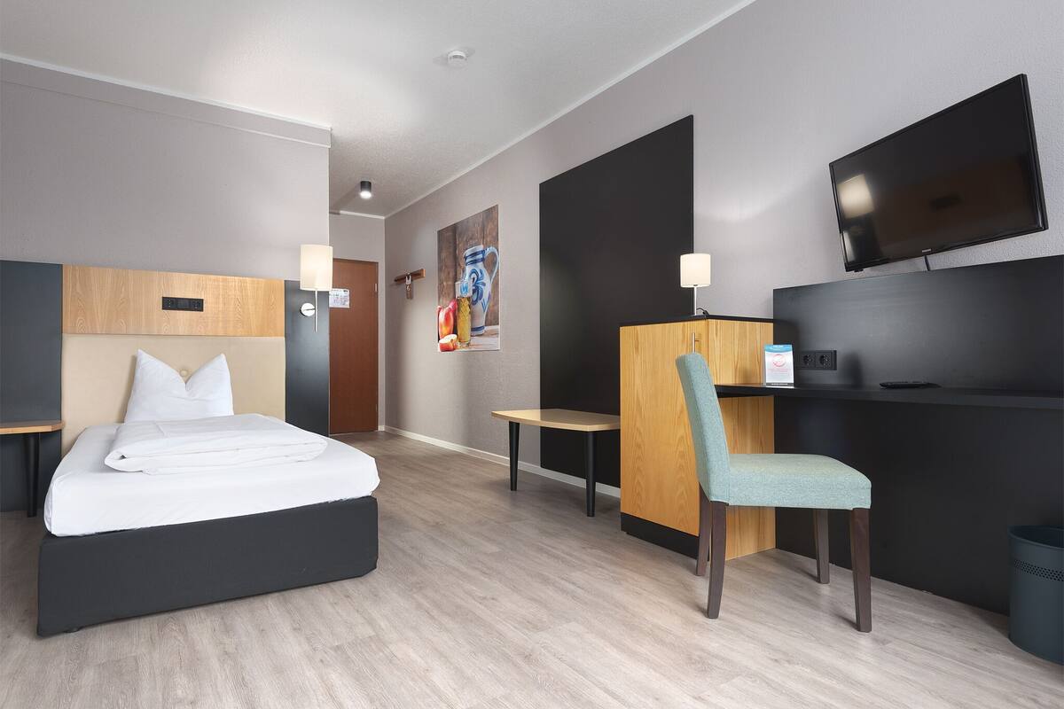 Une chambre d’hôtel moderne équipée d’un lit, d’un bureau, d’une chaise, d’un téléviseur et d’un autre téléviseur fixé au mur.