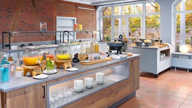 Un bar à petit-déjeuner moderne, avec un mur en briques, de grandes fenêtres et une grande variété d’aliments proposés pour le petit-déjeuner.