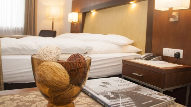 Habitación de hotel con una cama bien hecha, una mesita de noche con lámpara, un teléfono y una revista sobre la mesa.