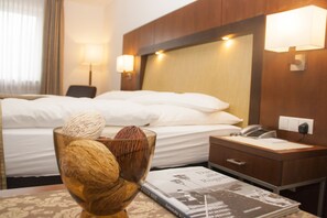 A hotel room with a neatly made bed, a bedside table with a lamp, a telephone, and a magazine on the table. - Hotel zum Adler (Bonn)