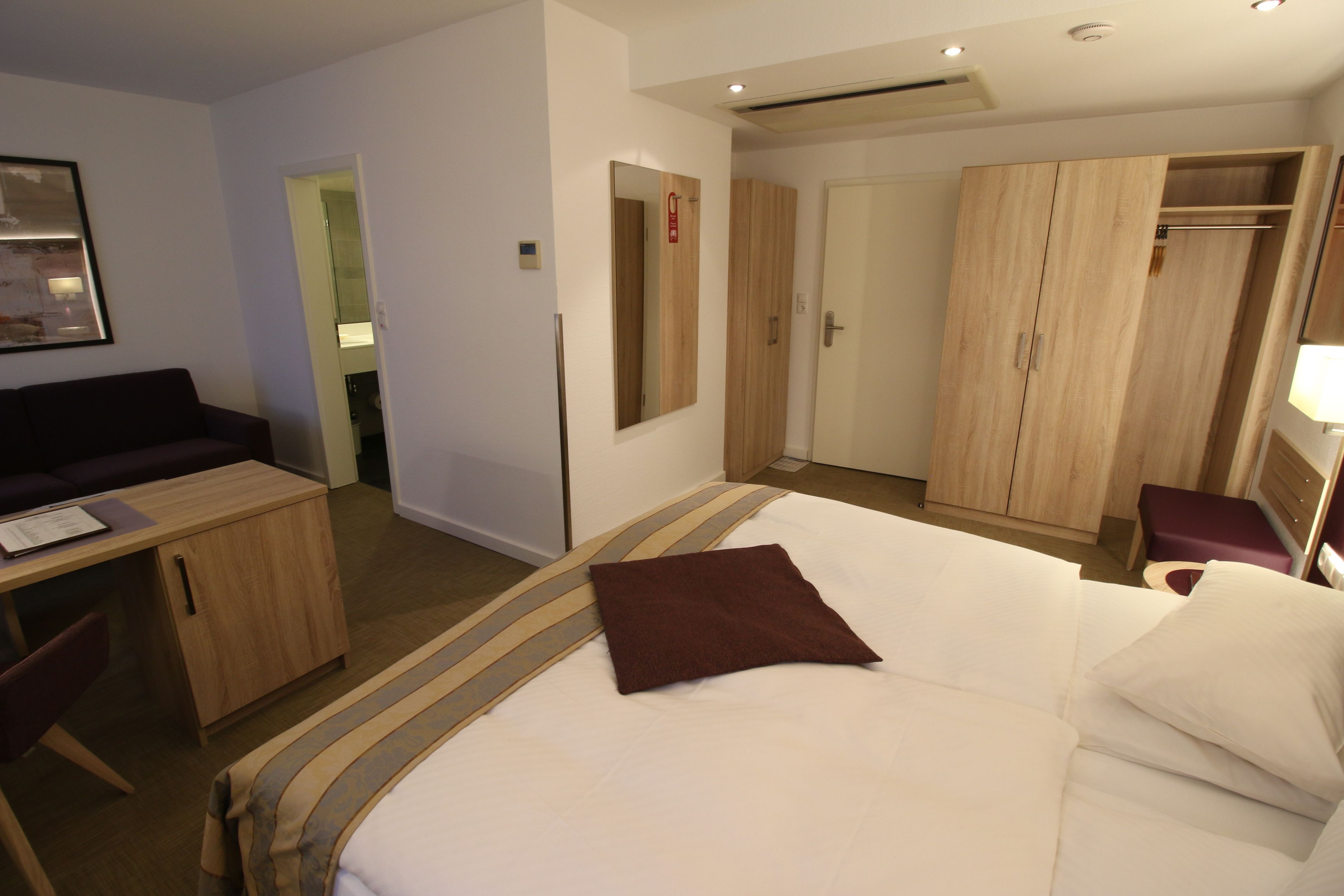 Habitación de hotel con cama, escritorio, armario y espejo.
