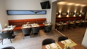 Un restaurante con varias mesas, un televisor grande de pared y una zona de estar con bancos acolchados naranja.
