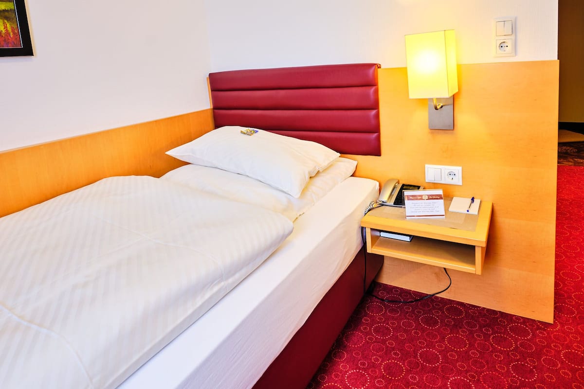 A hotel room with a bed, a nightstand with a lamp, a phone, and a sign.