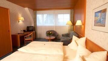 Habitación de hotel con una cama grande, un escritorio con televisor, una silla y una mesita de noche con lámpara.