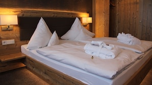 Ein ordentlich bezogenes Bett mit weißen Leinen und Kissen, ein Holz-Kopfbrett und ein Holzschrank mit Spiegel.