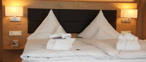 A hotel room with a wooden headboard, two bedside lamps, a neatly made bed with white linens, and a small bedside table with a cup and a book.