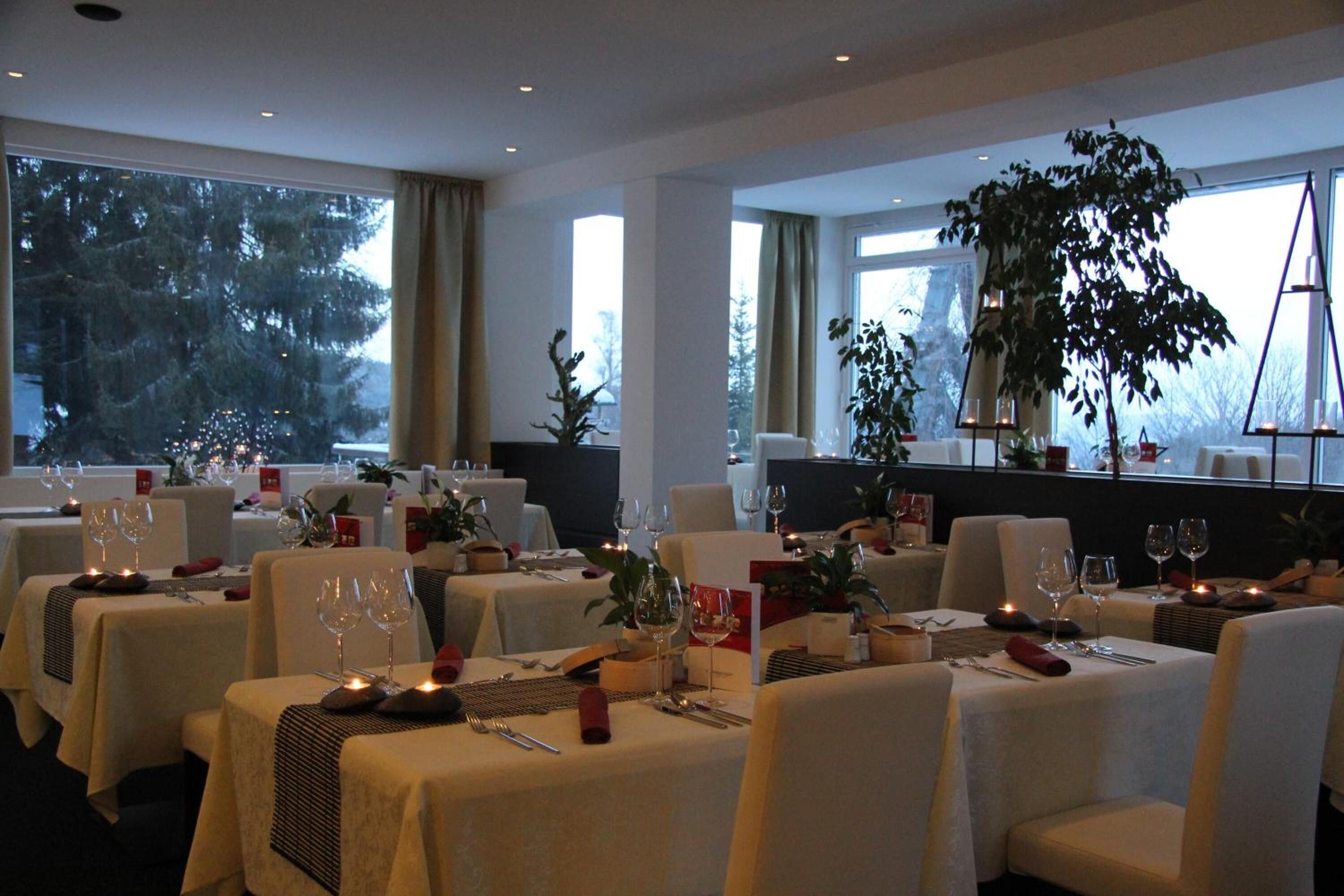 Ein Restaurant mit gedeckten Tischen, großen Fenstern und Zimmerpflanzen.