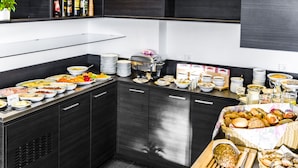 Ein reichhaltiges Buffet mit verschiedenen Speisen, einer Kaffeemaschine und einer Obstschale.