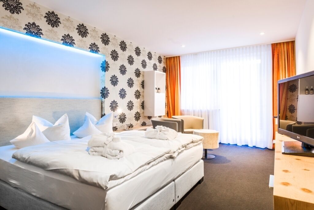 Une chambre d’hôtel avec un grand lit, une télévision, un bureau et une fenêtre avec des rideaux.