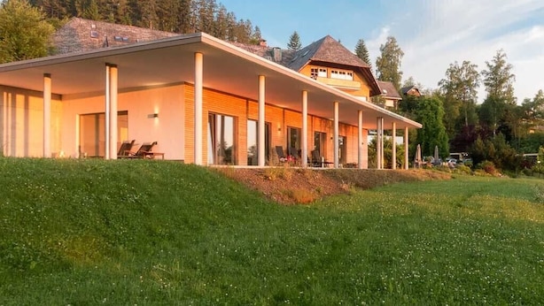 Ein modernes Haus mit überdachter Terrasse, großen Fenstern und einem grünen Rasen.