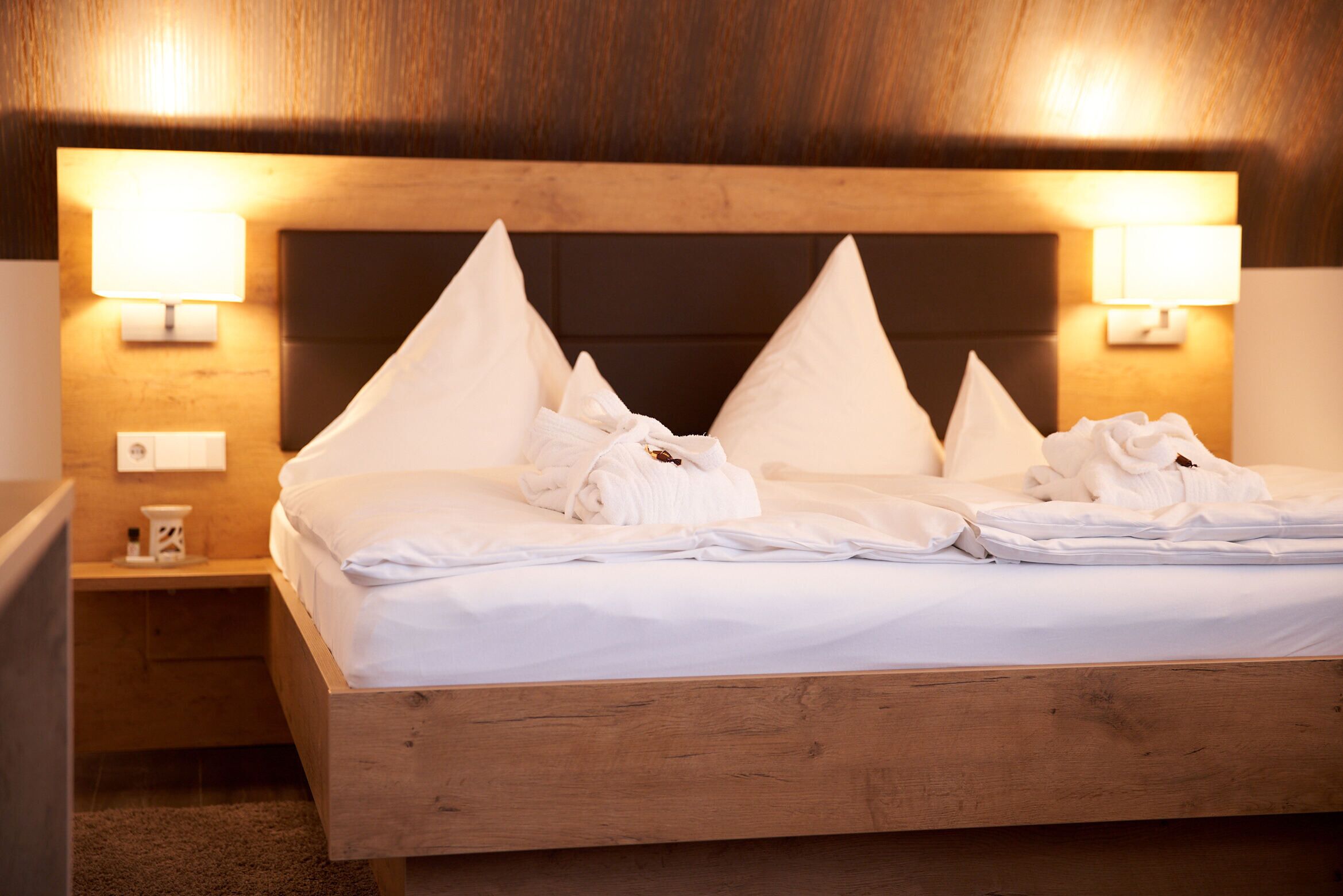 A neatly made bed with white linens and pillows, a wooden headboard, and two bedside lamps.