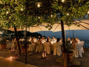 An outdoor dining area with tables and chairs under umbrellas, surrounded by greenery. - Hotel Villa Schuler (Taormina)