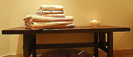A room with a table holding folded towels and a candle, and a woven basket underneath.