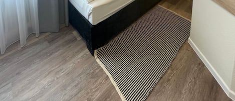 Habitación de hotel moderna con una cama individual, una mesita de noche, una lámpara de pared y un ventanal con cortinas.