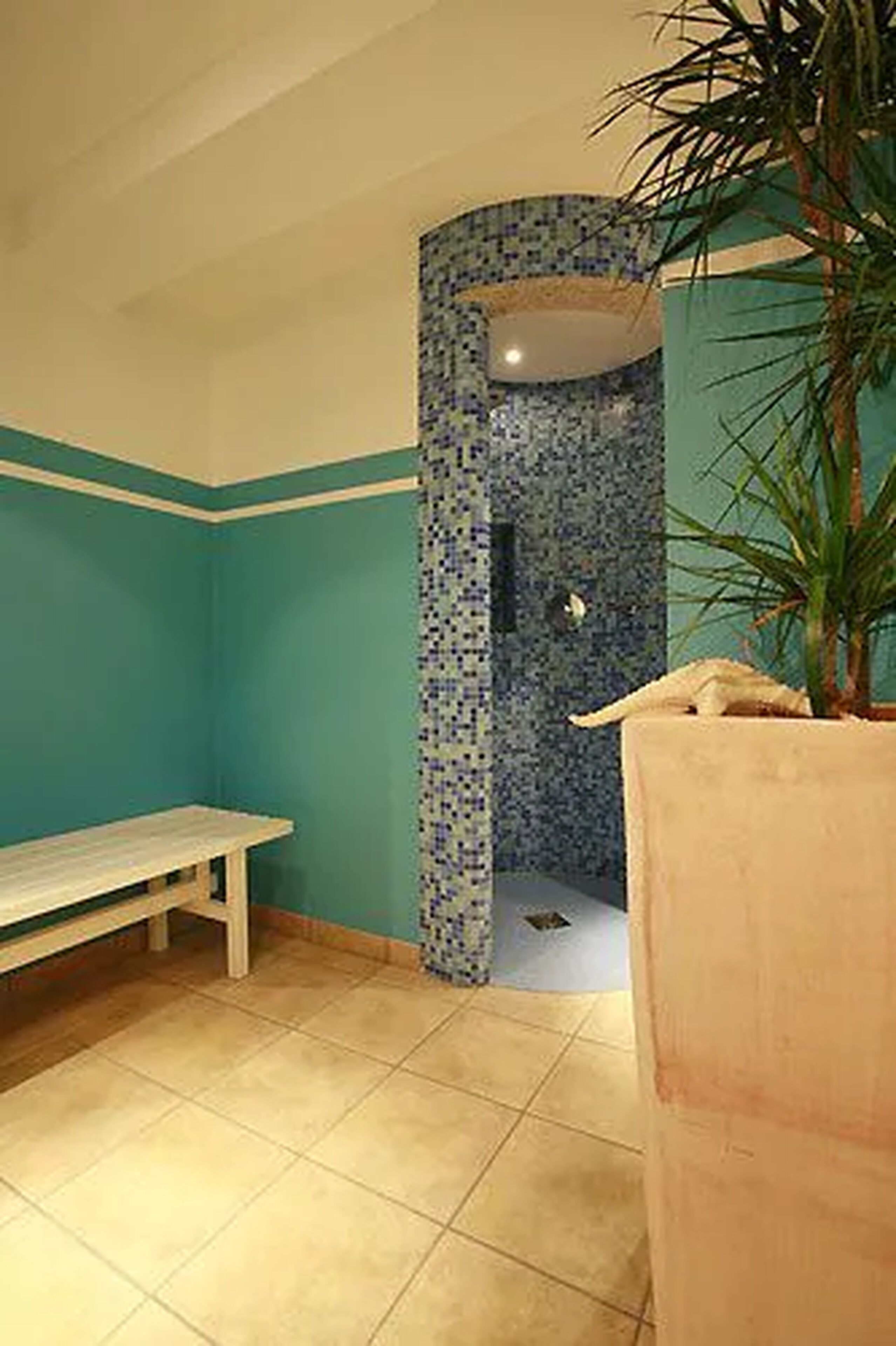 A bathroom with a bench, a shower with mosaic tile, and a potted plant.
