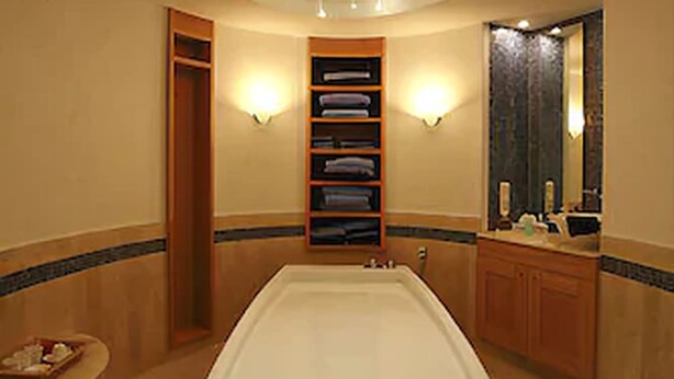 A modern bathroom with a central bathtub, a built-in shelf with towels, and a large mirror above the sink. - Hotel Faldernpoort (Emden)