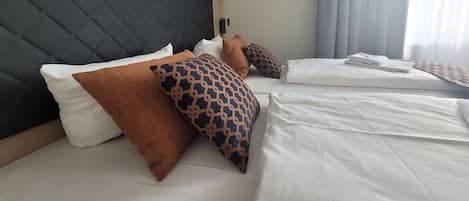 Una habitación de hotel con una cama grande, varios almohadones, un cabecero oscuro y una ventana con cortinas.