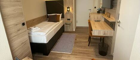 Una habitación de hotel moderna con cama, escritorio, silla, televisor y baño.