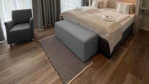 A modern bedroom with a large bed, a grey armchair, and a striped rug. - Hotel Faldernpoort (Emden)