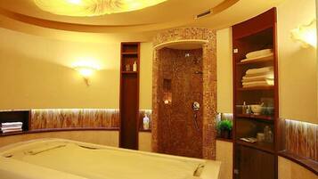 A spa room with a massage table, a shower area with a tiled wall, and a wooden cabinet with towels.
