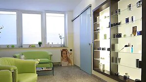 A room with a green sofa, a large window, a wall-mounted shelf with items, and a door. - Hotel Faldernpoort (Emden)