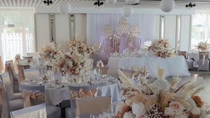 A banquet hall with round tables set for a formal event, featuring white tablecloths, elegant floral centerpieces, and neatly arranged silverware. - Hotel Faldernpoort (Emden)