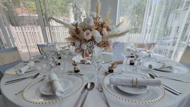 A round table set with white tablecloths, gold accents, and a floral centerpiece. - Hotel Faldernpoort (Emden)