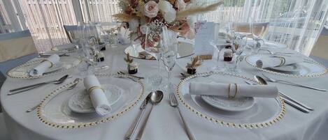A round table set with white tablecloths, gold accents, and a floral centerpiece.