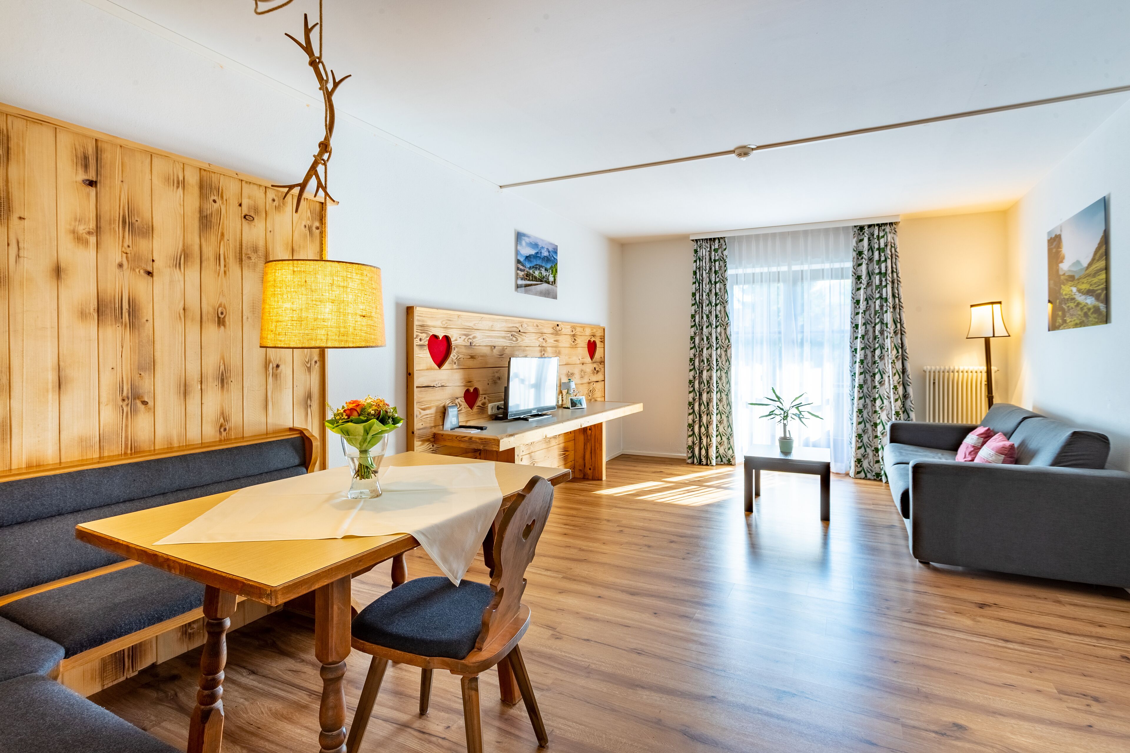 A modern living room with a wooden bench, a dining table with a vase of flowers, a sofa, a coffee table, and a TV on a wooden stand.