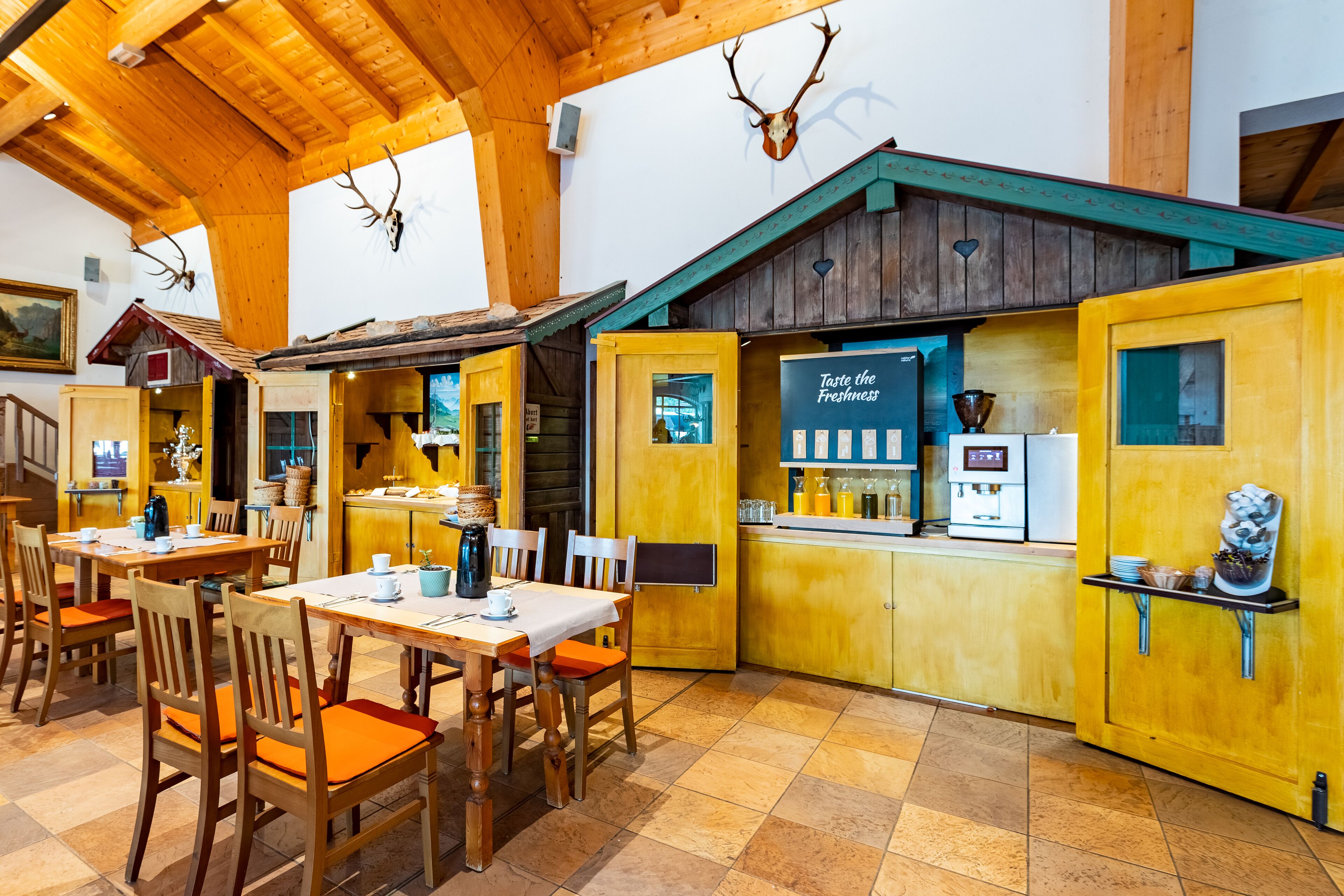 A restaurant with wooden interiors, a bar area, and a sign that reads "Taste the Freshness."