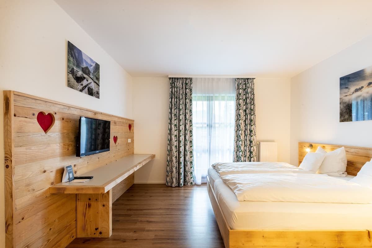 Une chambre d’hôtel avec un lit en bois, un téléviseur posé sur un meuble en bois, un bureau et une fenêtre avec des rideaux.