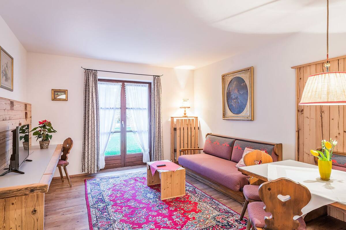 Un salon confortable avec un canapé, une petite table et une table à manger avec des chaises. On y trouve une cheminée, une fenêtre avec des rideaux et une lampe.