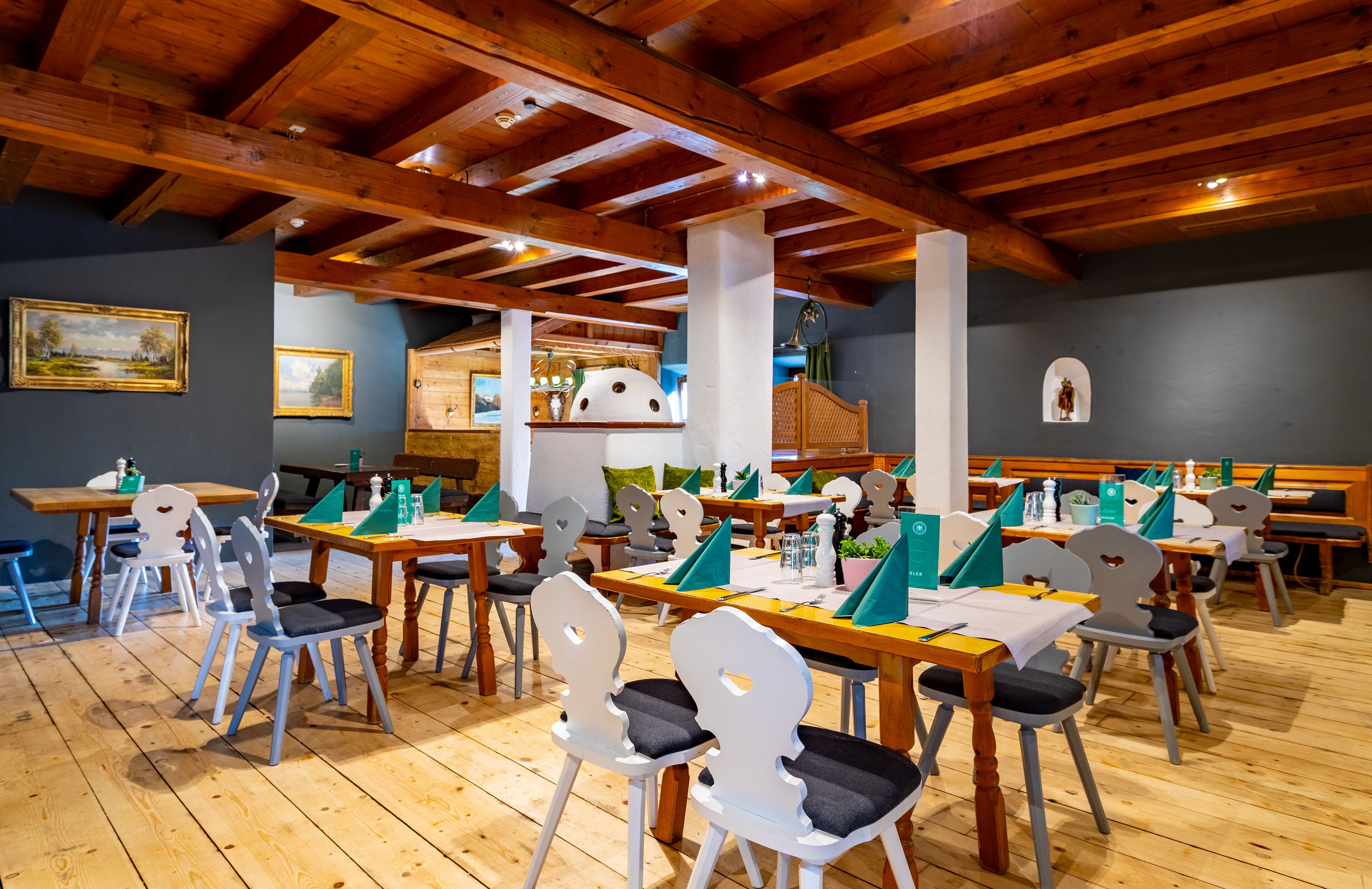 A restaurant with wooden tables and chairs, a high ceiling with exposed beams, and a view of the kitchen in the background.