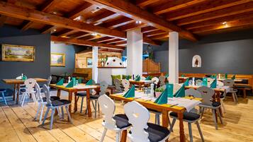 A restaurant with wooden tables and chairs, a high ceiling with exposed beams, and a view of the kitchen in the background.