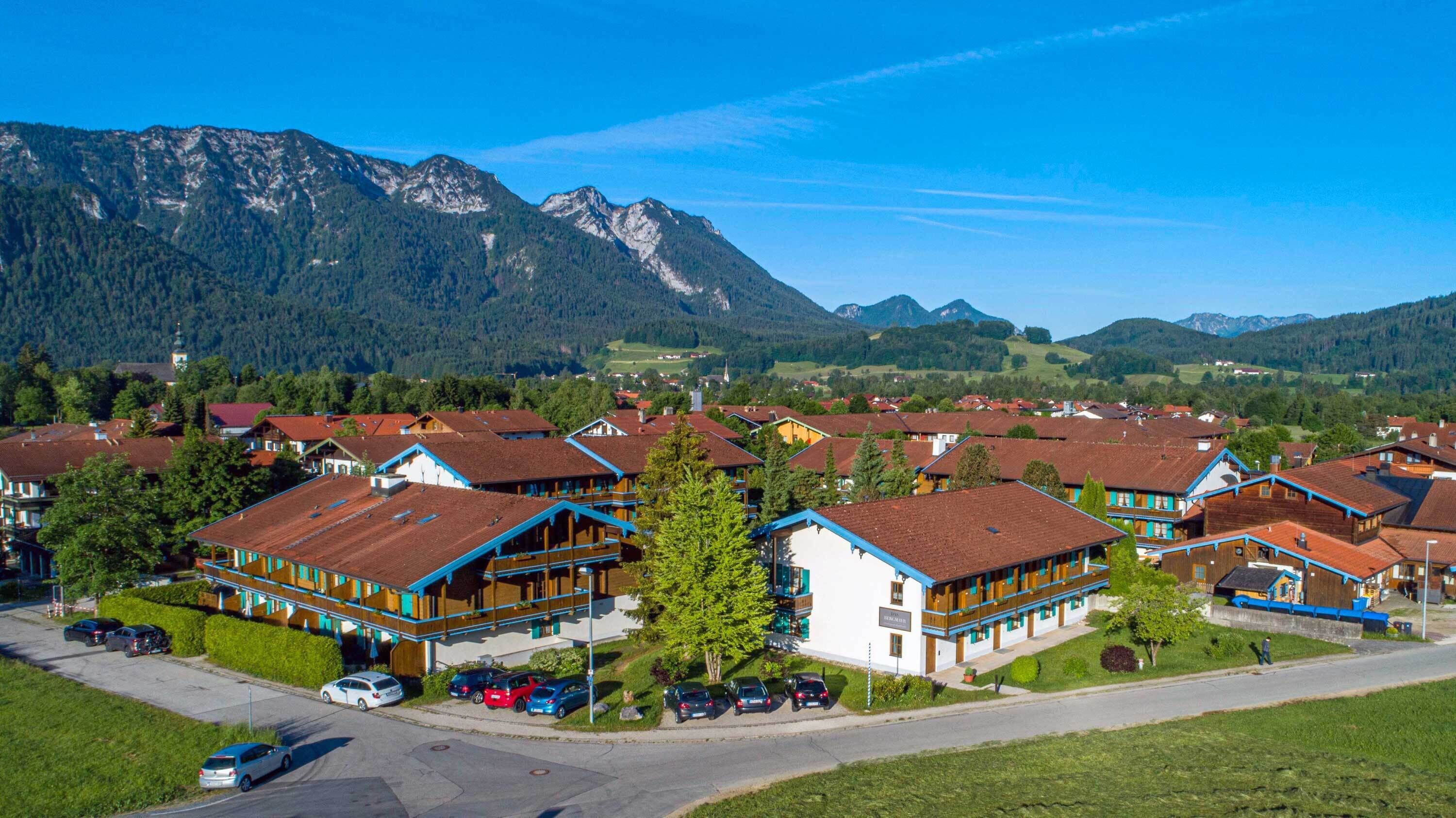 A cluster of traditional wooden houses with sloped roofs, surrounded by lush greenery and mountains in the background.