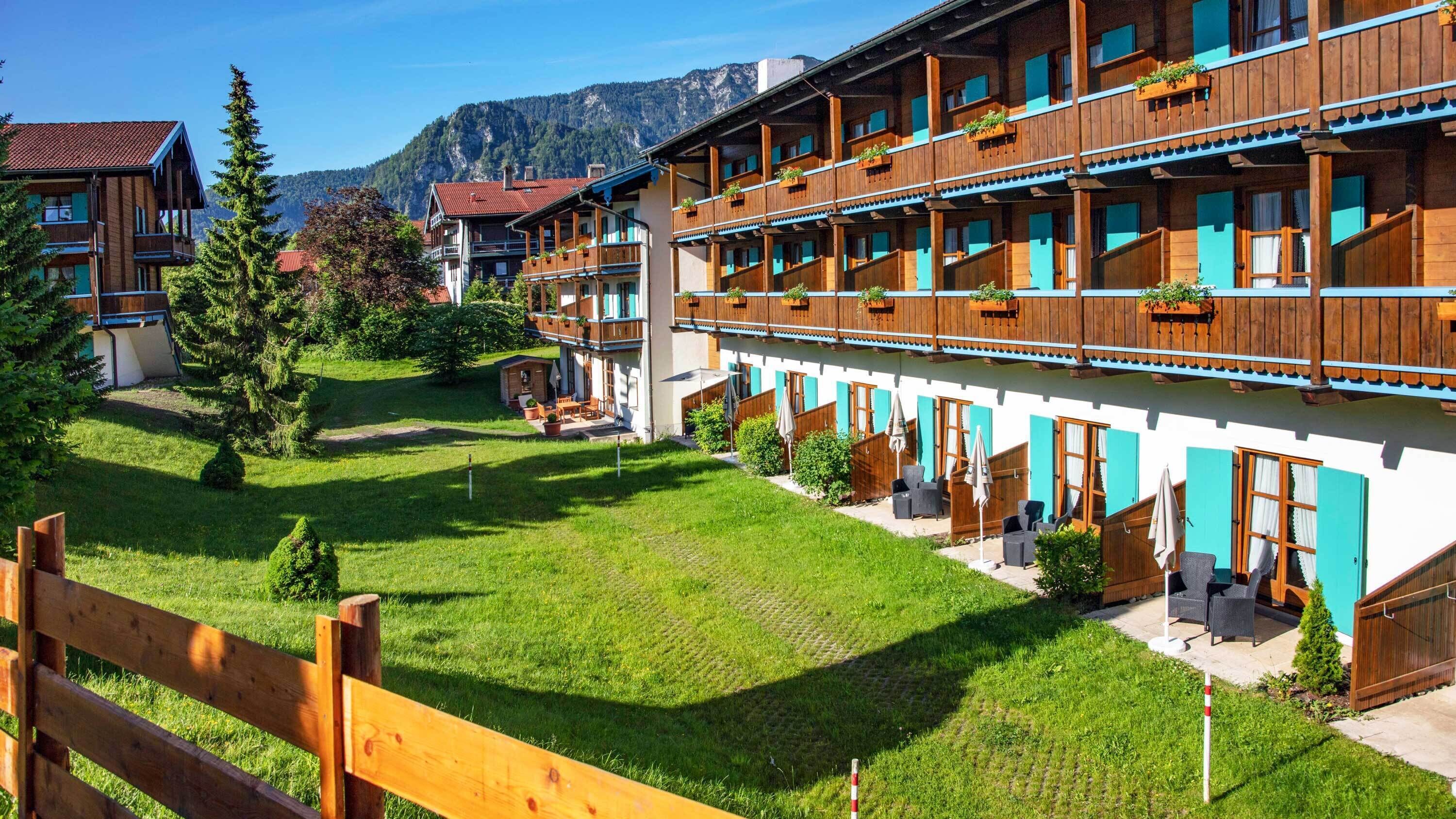 Un hotel con varios balcones, mobiliario exterior y montañas al fondo.