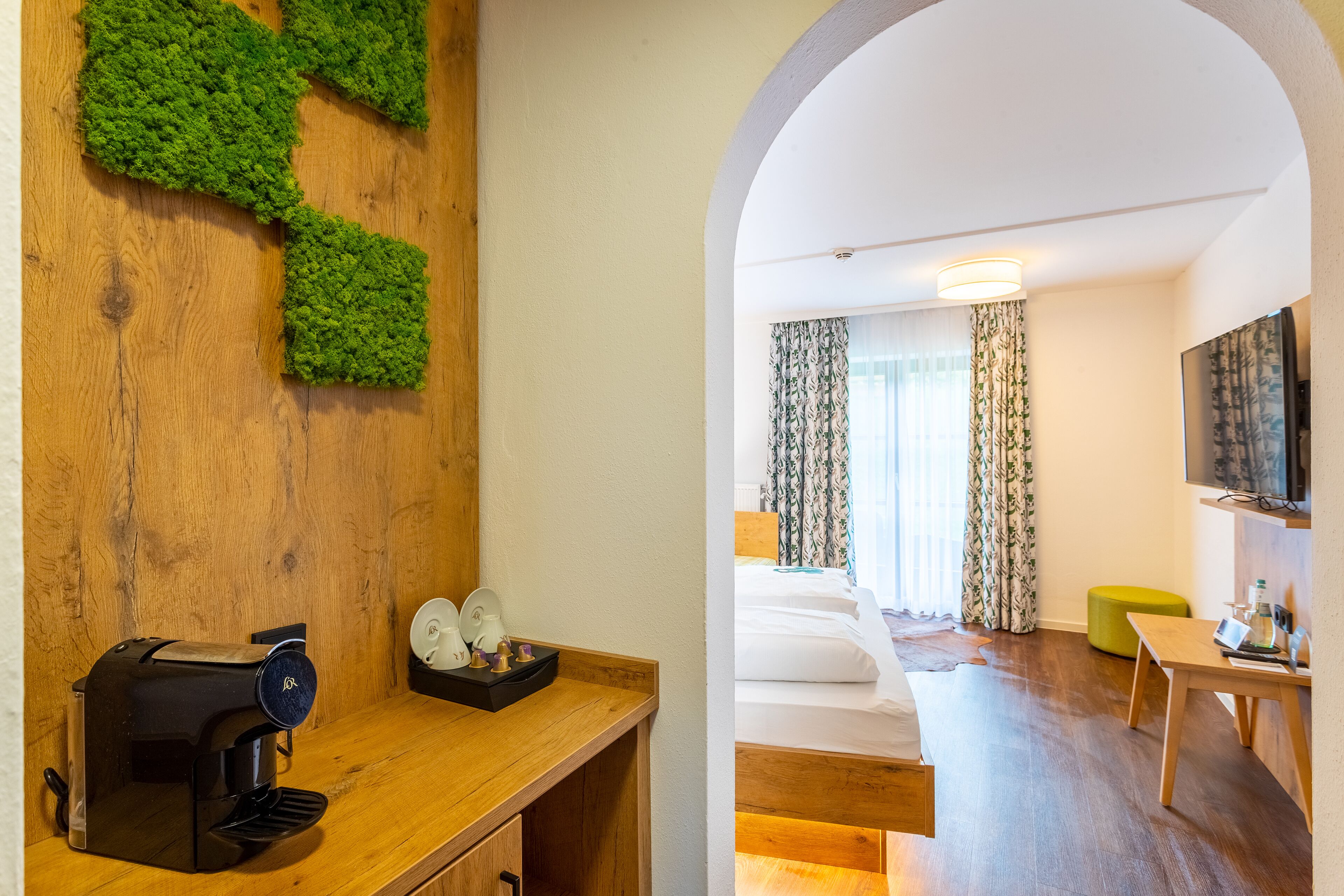 Ein Hotelzimmer mit einem Holztisch, einer Kaffeemaschine und einer grünen Wanddekoration.