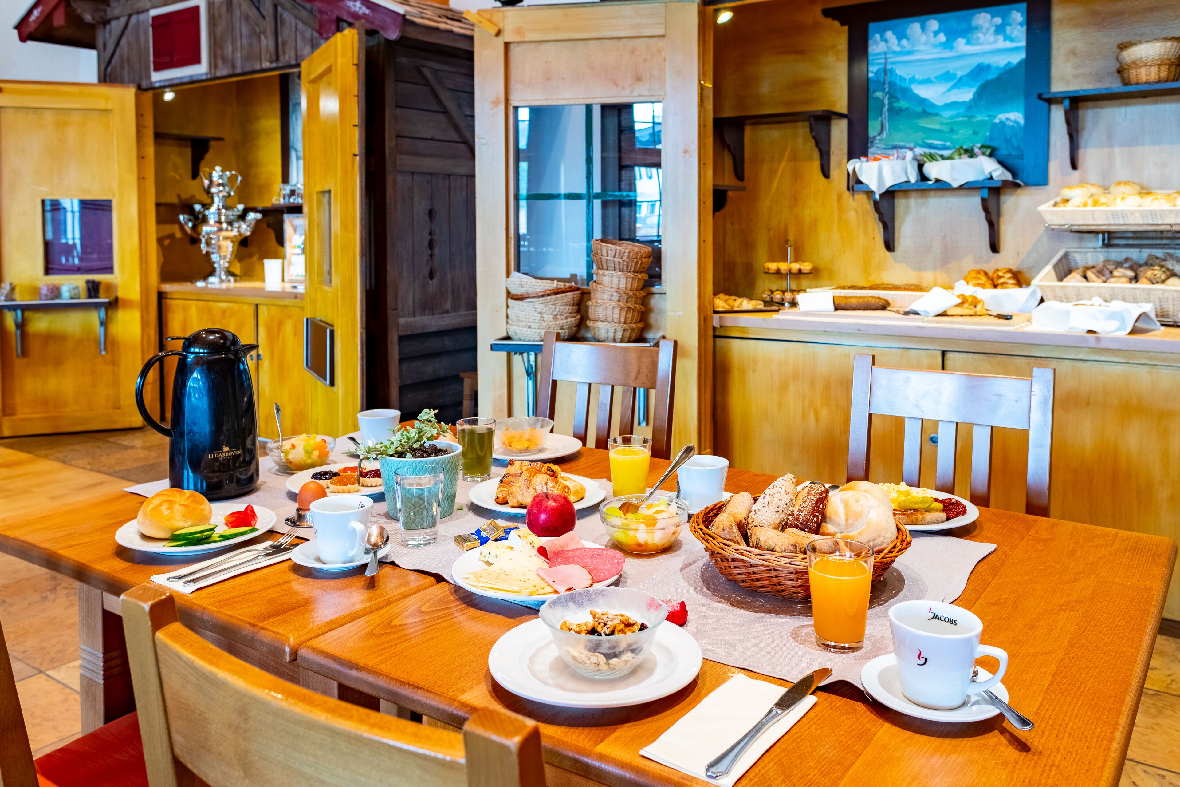 A breakfast setting with a wooden table, various breakfast items, and a coffee maker.