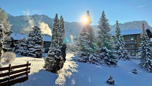 Schneebedeckte Landschaft mit einer hölzernen Bank, immergrünen Bäumen und einem Gebäude mit geneigtem Dach.