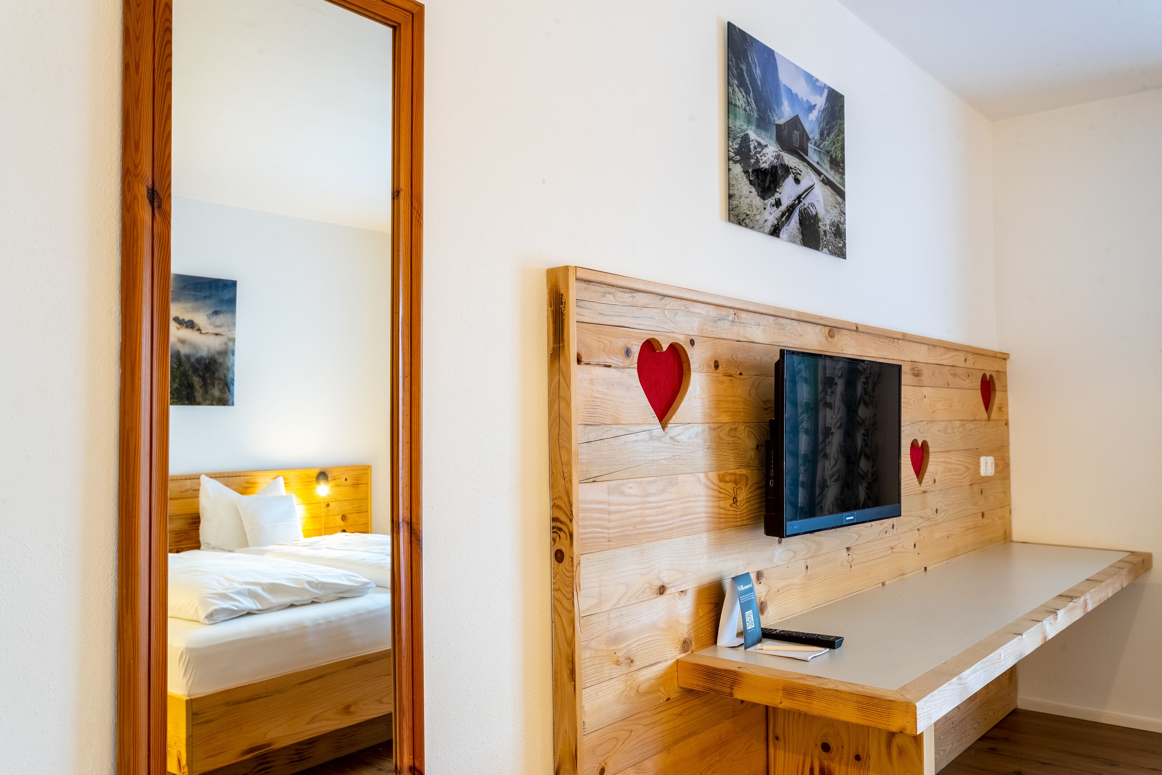 A hotel room with a wooden headboard, a bed with white linens, a mounted TV, and a small bedside table.