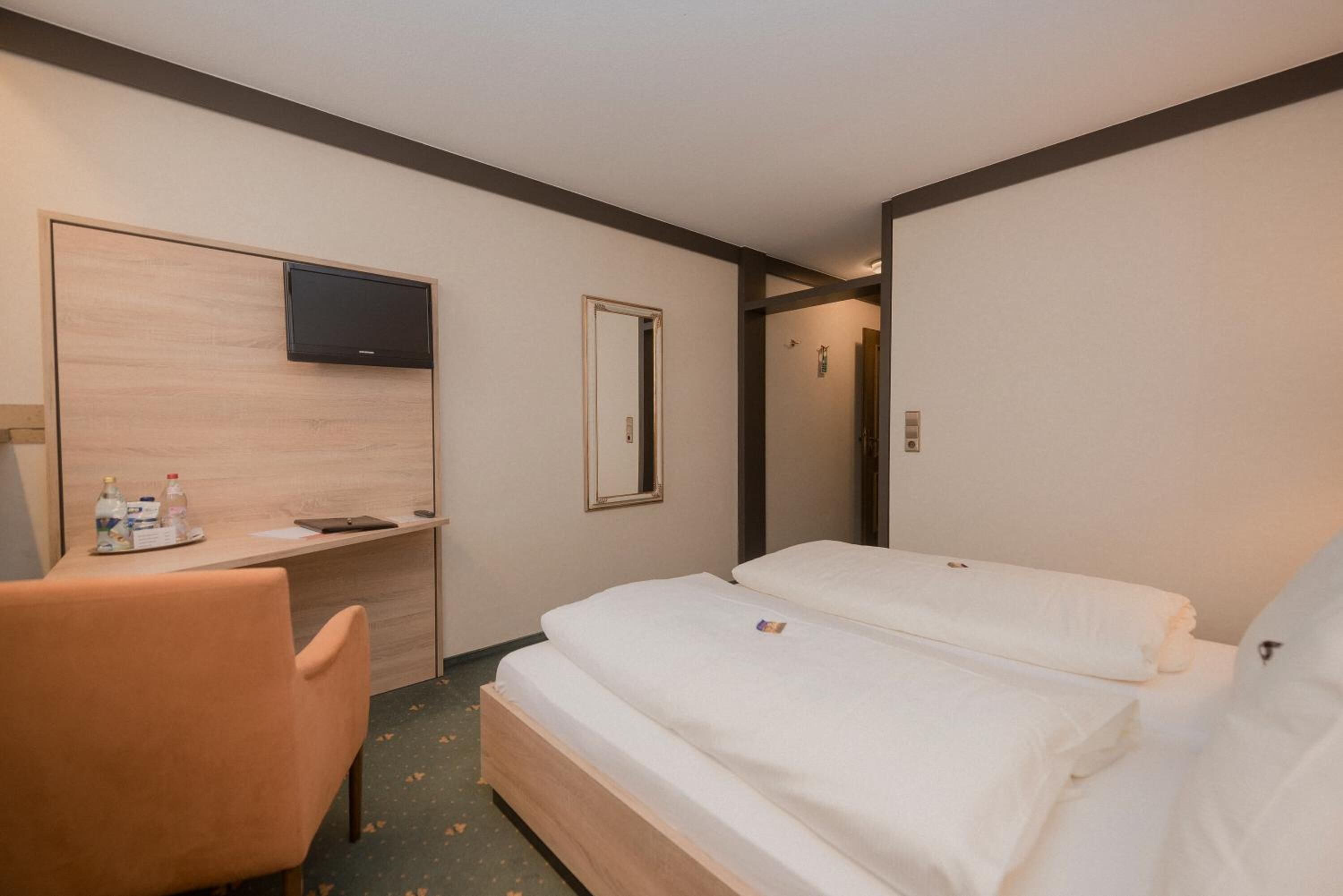 A hotel room with a bed, a desk, a chair, a television, and a mirror.
