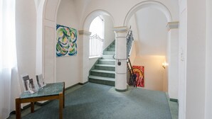Ein Flur mit einer Treppe, einem Glastisch mit Broschüren und zwei abstrakten Gemälden.