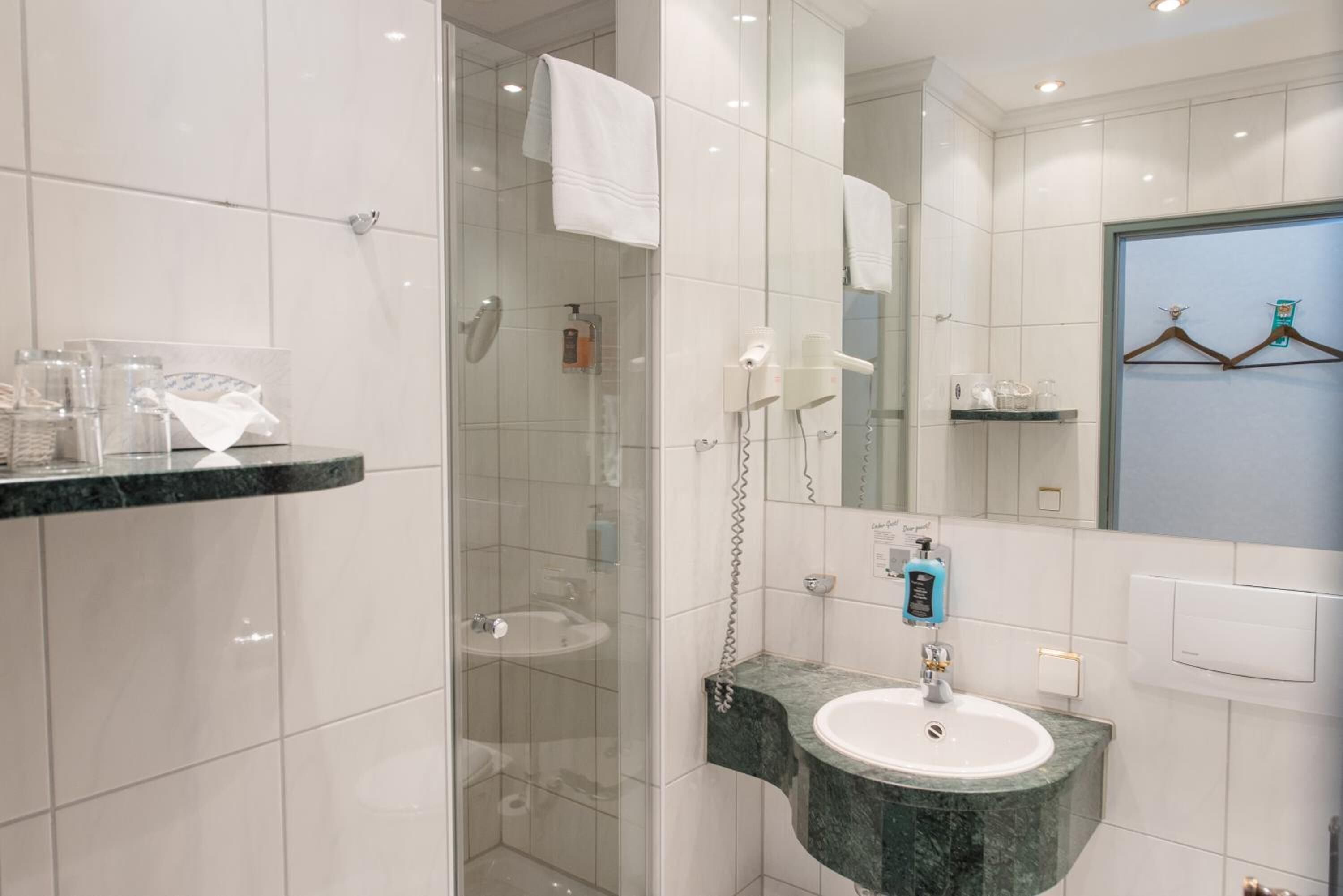 A modern bathroom with a glass-enclosed shower, a marble sink, and a mirror with a towel rack.