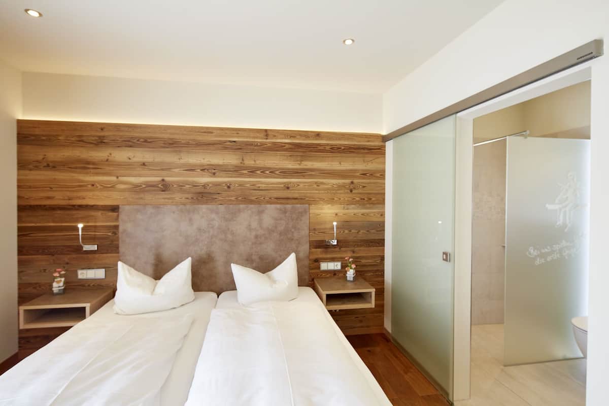 A bedroom with a wooden headboard, two bedside tables with lamps, and a sliding door to the bathroom.