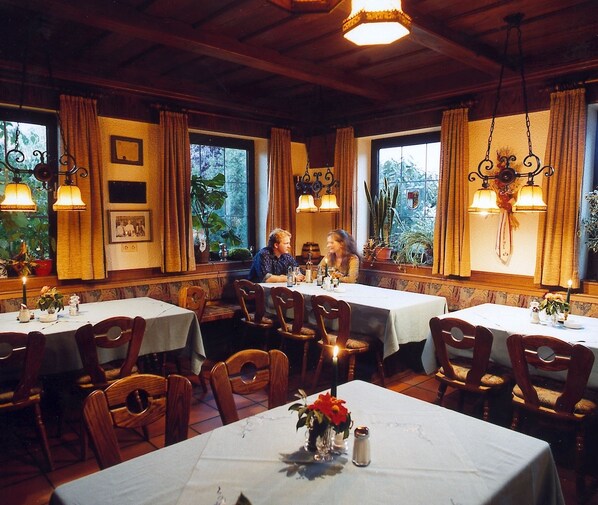 A restaurant with wooden tables and chairs, hanging light fixtures, and large windows with curtains. - Landgasthof Fiedler (Dietersheim)