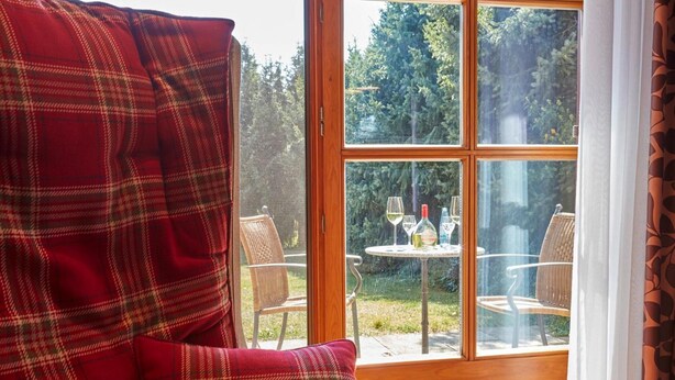 A room with a plaid-patterned chair and a view of an outdoor table with chairs and a glass of wine. - Landgasthof Fiedler (Dietersheim)