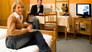 A room with a bed, a wooden chair, a table with a laptop, and a television. - Landgasthof Fiedler (Dietersheim)